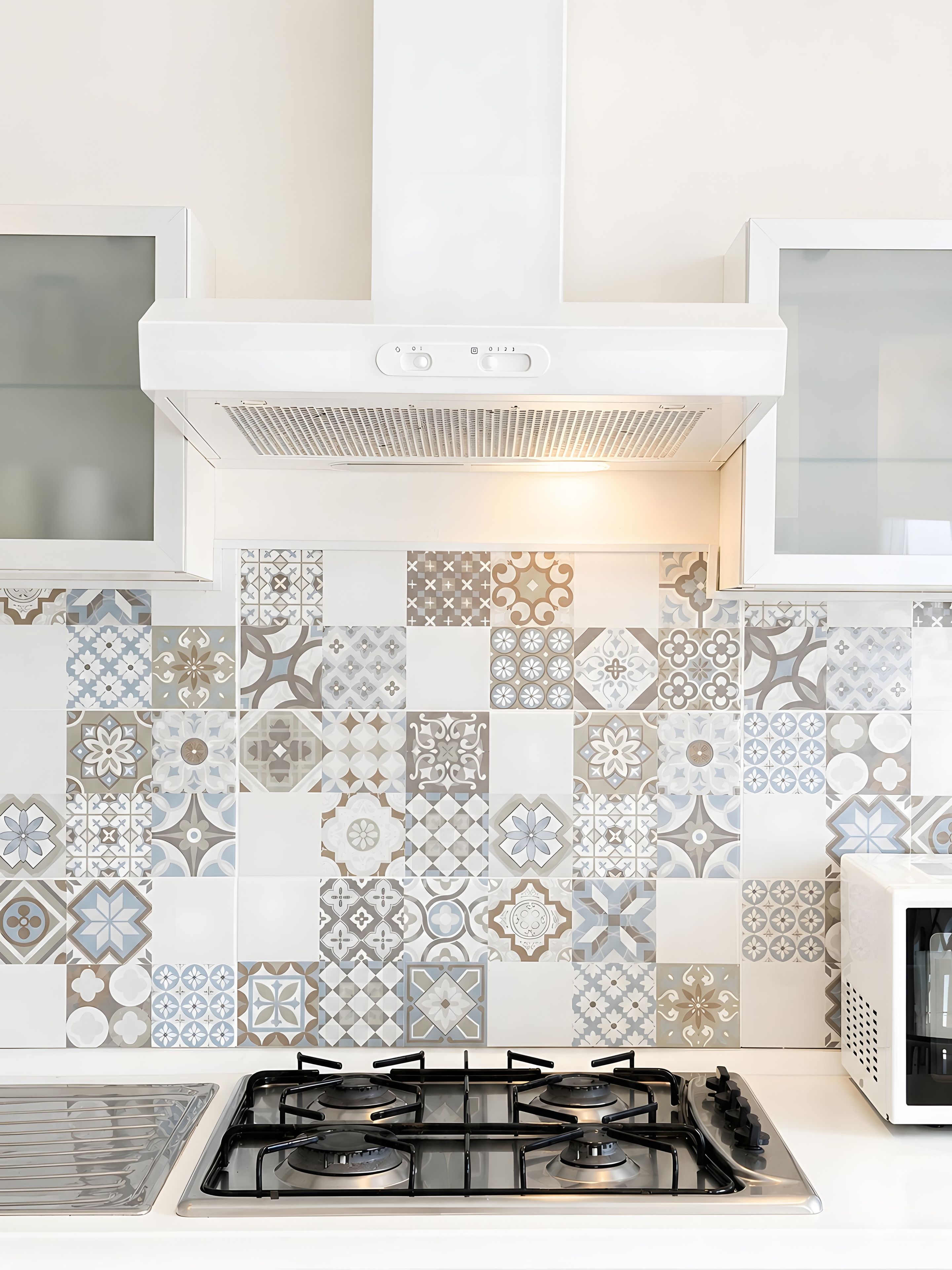 Een keuken met een gasfornuis, witte kastjes en betegelde spatwand.