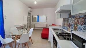 Una cocina funcional con una mesa, sillas, un reposapiés rojo, estufa y microondas.