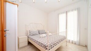 A bedroom with a bed, nightstand, and a window with curtains. - Apartment 'A 104 Puntavilla' – Perfect for Large Families (La Maddalena)