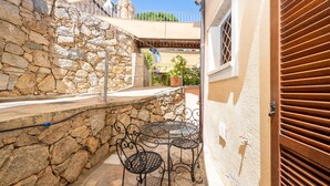 A stone wall, a metal table and chair, a potted plant, and a wooden door. - Apartment 'A 104 Puntavilla' – Perfect for Large Families (La Maddalena)