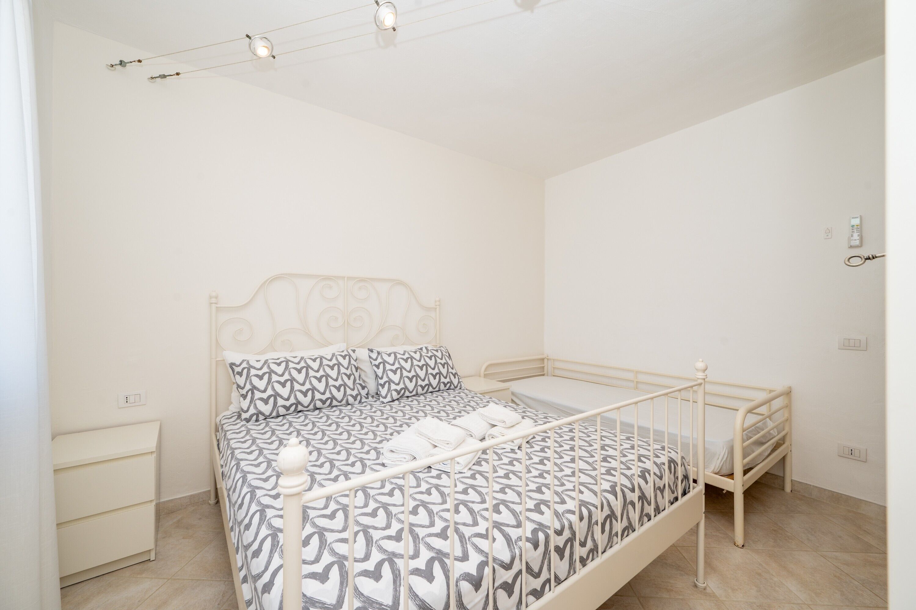 Une chambre avec un lit simple, une couvre-lit à motifs, une table de chevet et une petite table de nuit.