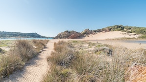 A sandy beach path leading to a rocky area with sparse vegetation. - Apartment 'A 104 Puntavilla' – Perfect for Large Families (La Maddalena)