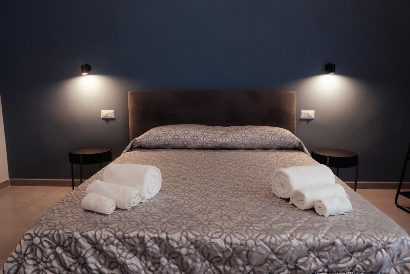 Une chambre d’hôtel avec un grand lit, deux tables de chevet et des lampes fixées au mur.