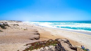 Ein Strand mit blauem Himmel, sandigem Gelände und Wellen.