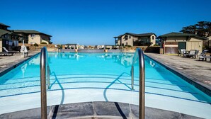 Une piscine à l’eau d’un bleu cristallin, entourée de chaises longues et bordée d’une terrasse en pierre.