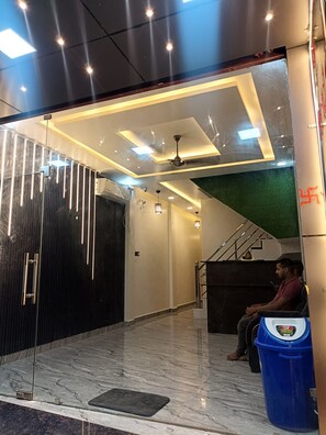 A modern reception area with a marble floor, a ceiling fan, and a staircase leading to an upper level. - Gita Raman Palace (Ayodhya)