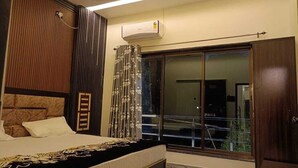 A bedroom with a bed, a window with curtains, an air conditioning unit, and a wardrobe. - Gita Raman Palace (Ayodhya)