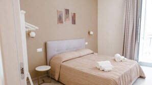 Quarto de hotel com uma cama, uma mesa redonda pequena e uma janela com cortinas.