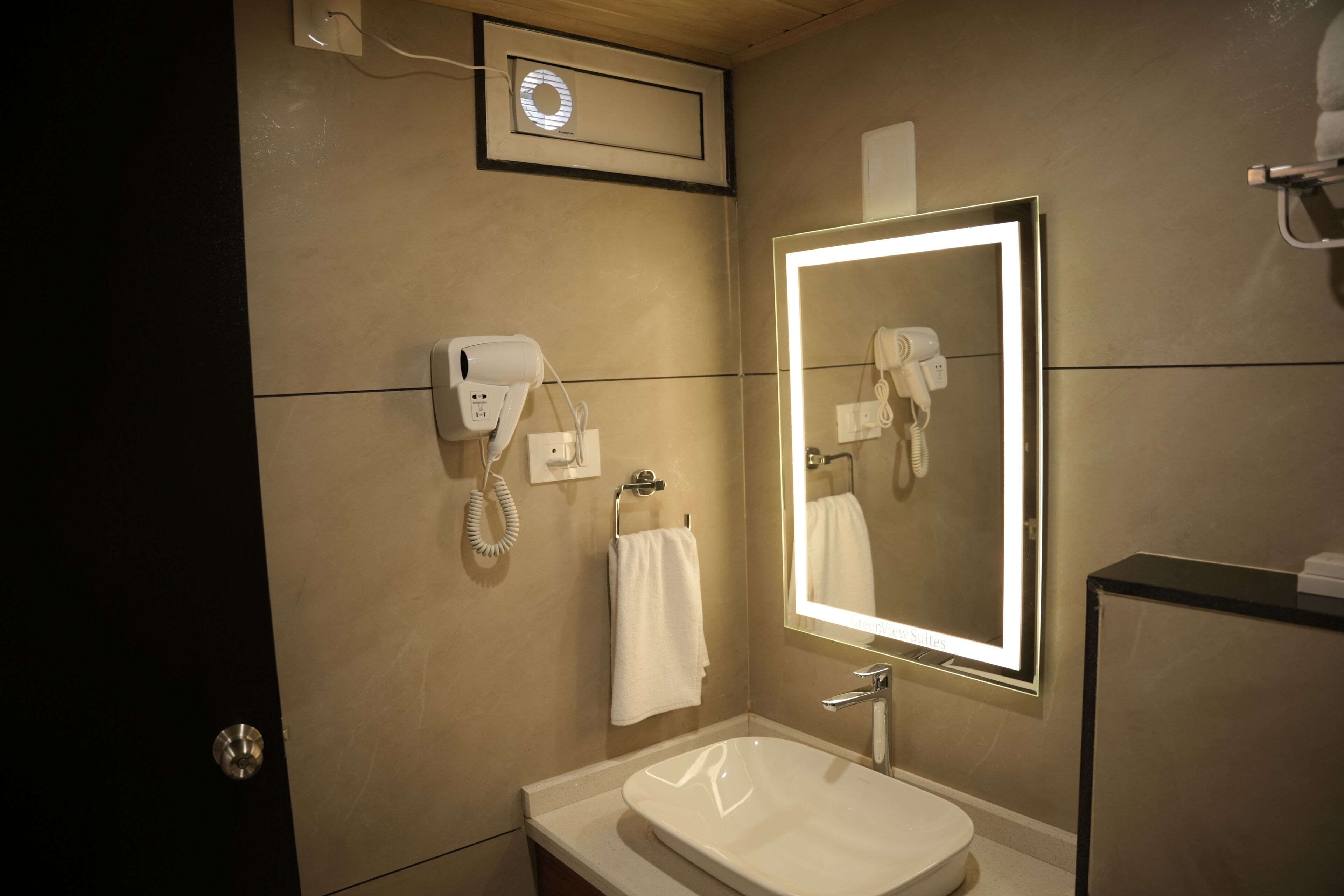 Un baño con lavamanos, espejo, secador de pelo y toallero.