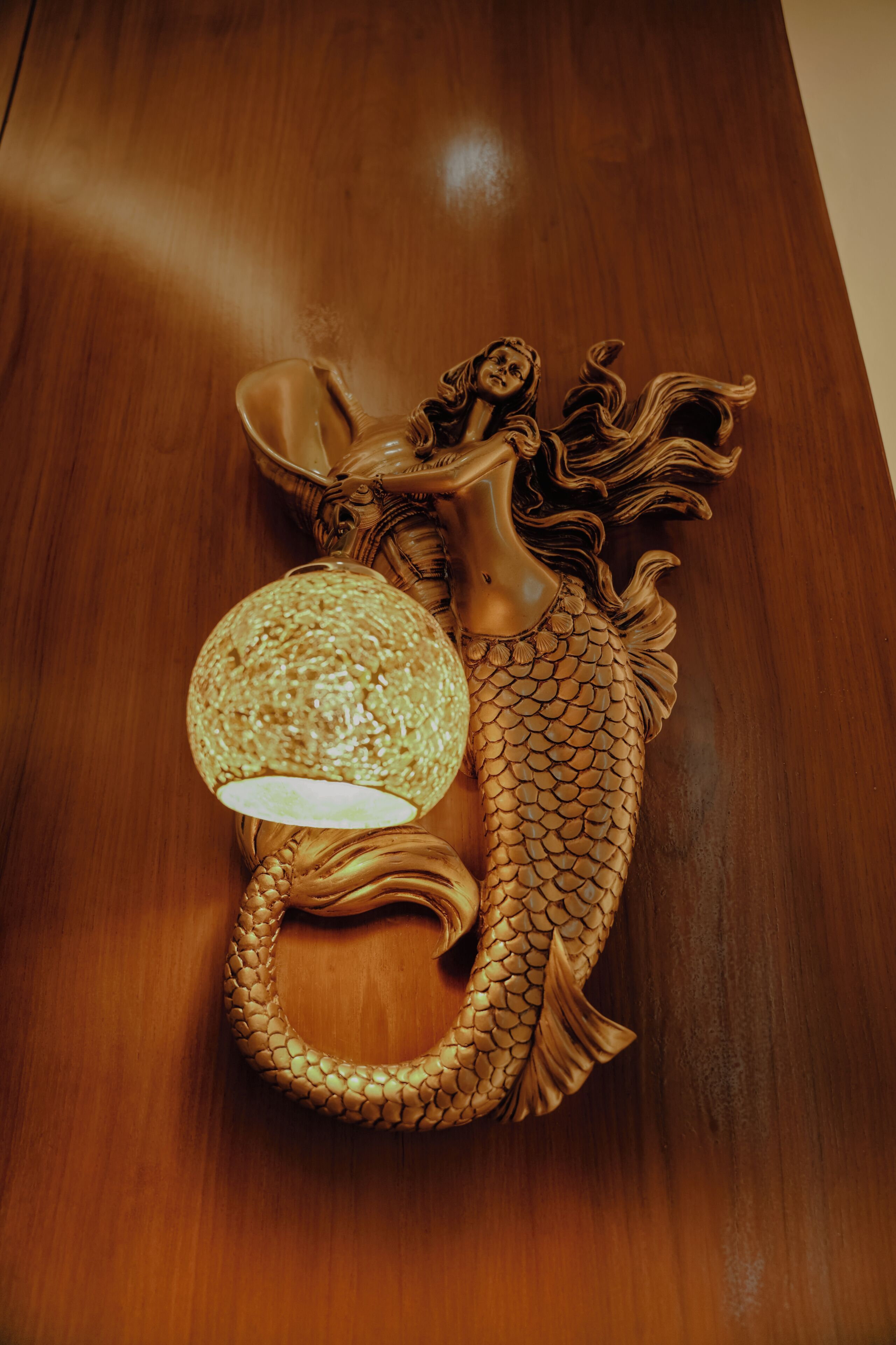 A wooden table with a decorative lamp and a mermaid figure.