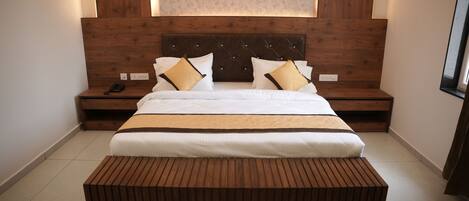 Un dormitorio moderno con cabecera de madera, una cama grande con ropa de cama blanca, dos mesitas de noche y un banco de madera en el centro.
