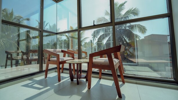 Ein Zimmer mit großen Fenstern, einem runden Tisch und zwei Holzsesseln.