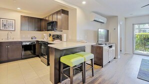 A modern kitchen with dark cabinets, a central island with stools, a built-in oven, and a large window. - Two 2BR Condos, Pool, Hot Tub, Prime location (Kailua-Kona)