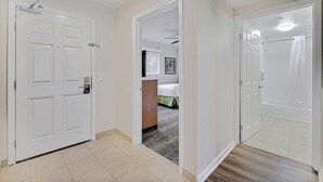 A hallway with white doors, a bed with green bedding, and a small desk with a chair. - Two 2BR Condos, Pool, Hot Tub, Prime location (Kailua-Kona)