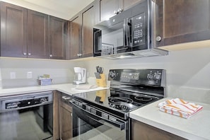 A modern kitchen with dark wooden cabinets, a black stove, and a microwave. - 2BR on Ironman Run Route, Pool & Hot Tub Access (Kailua-Kona)