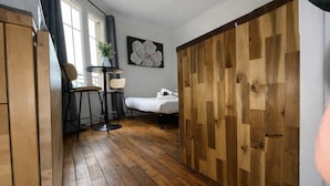 A room with a bed, a small table with chairs, a potted plant, and a wooden partition. - Studio Charmant Paris 15eme Proche Metro (Paris)