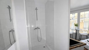 A modern bathroom with a glass-enclosed shower, white tiled walls, and a small table with chairs by a window. - Studio Charmant Paris 15eme Proche Metro (Paris)