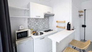 Uma cozinha compacta com armários brancos, painel decorativo e eletrodomésticos como micro-ondas, pia e geladeira pequena.