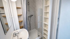 Uma casa de banho moderna com cabine de chuveiro em vidro, uma pia branca e prateleiras embutidas.