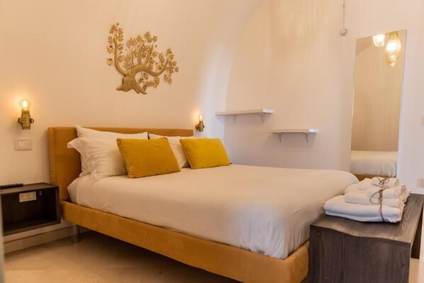 A bed with white and yellow bedding, a nightstand, a wall-mounted lamp, a mirror, and a towel rack. - DOMUS SAN GIOVANNI (Locorotondo)