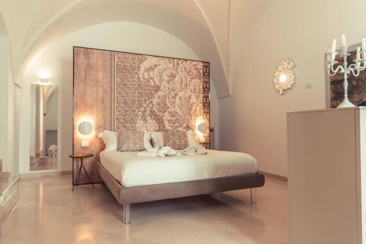 A modern bedroom with a large bed, a decorative headboard, two bedside lamps, and a mirror.