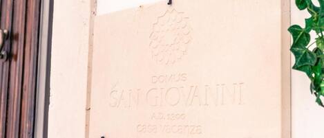 Eine Tafel mit der Inschrift 'DOMUS SAN GIOVANNI A.D. 1300 casa vacanza' an einer Wand befestigt.