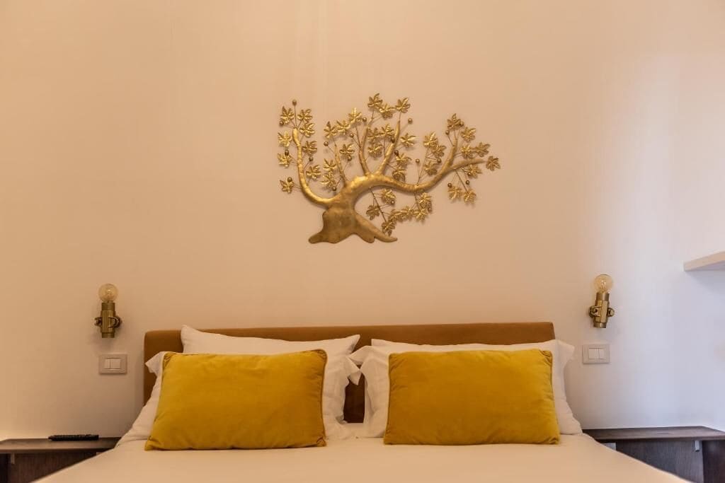 Ein Bett mit weißer und gelber Bettwäsche, ein an der Wand befestigter Baumschmuck und Nachttischlampen.