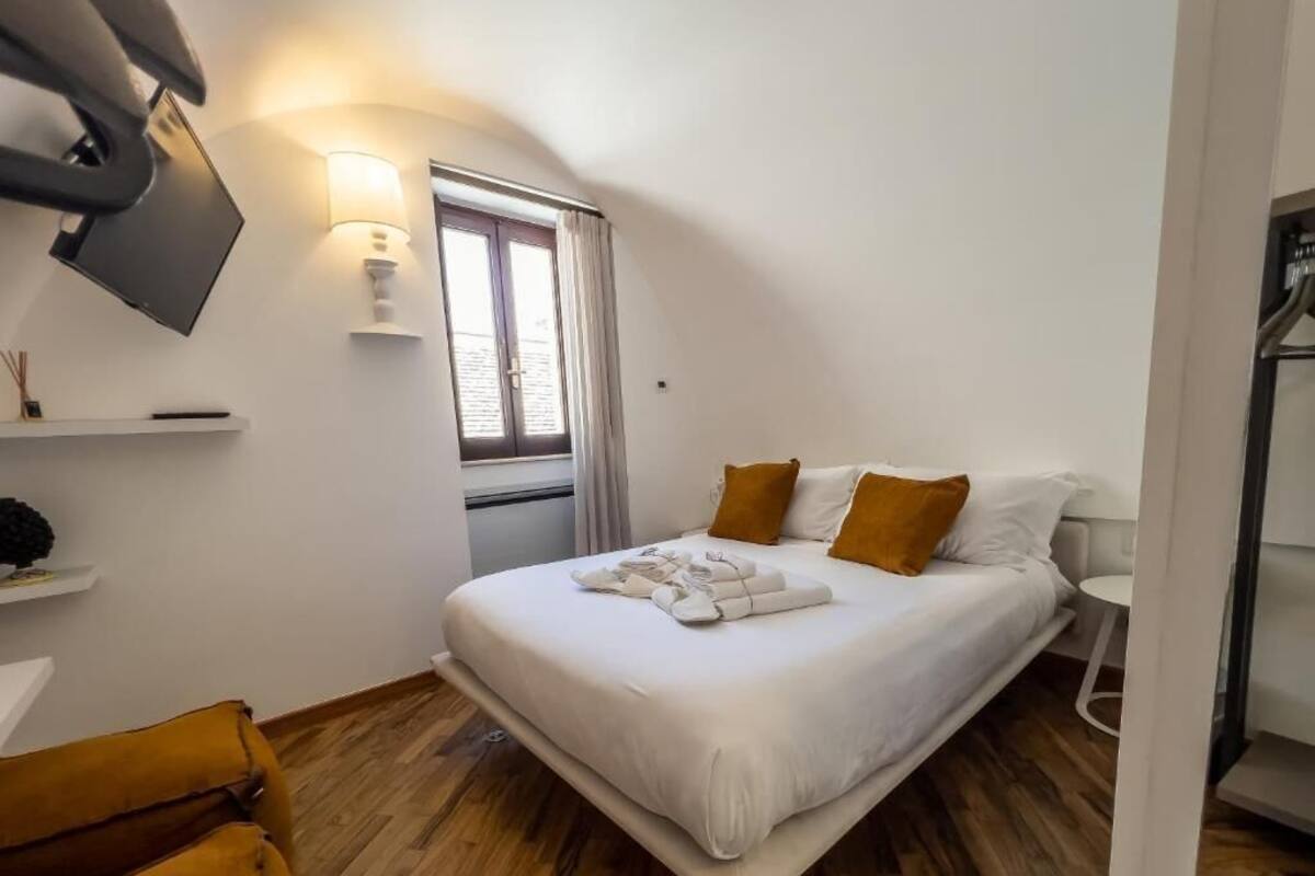 A bedroom with a bed, a TV mounted on the wall, a window with curtains, and a wooden floor.