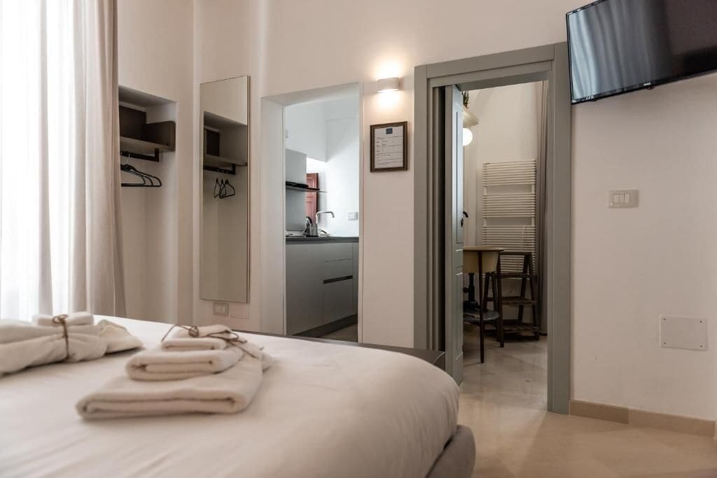 A hotel room with a bed, a bathroom, a kitchenette, and a TV mounted on the wall.