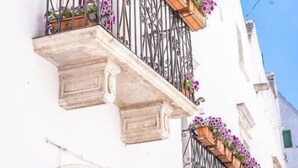 A white building with balconies adorned with wooden planters and purple flowers. - DOMUS SAN GIOVANNI (Locorotondo)
