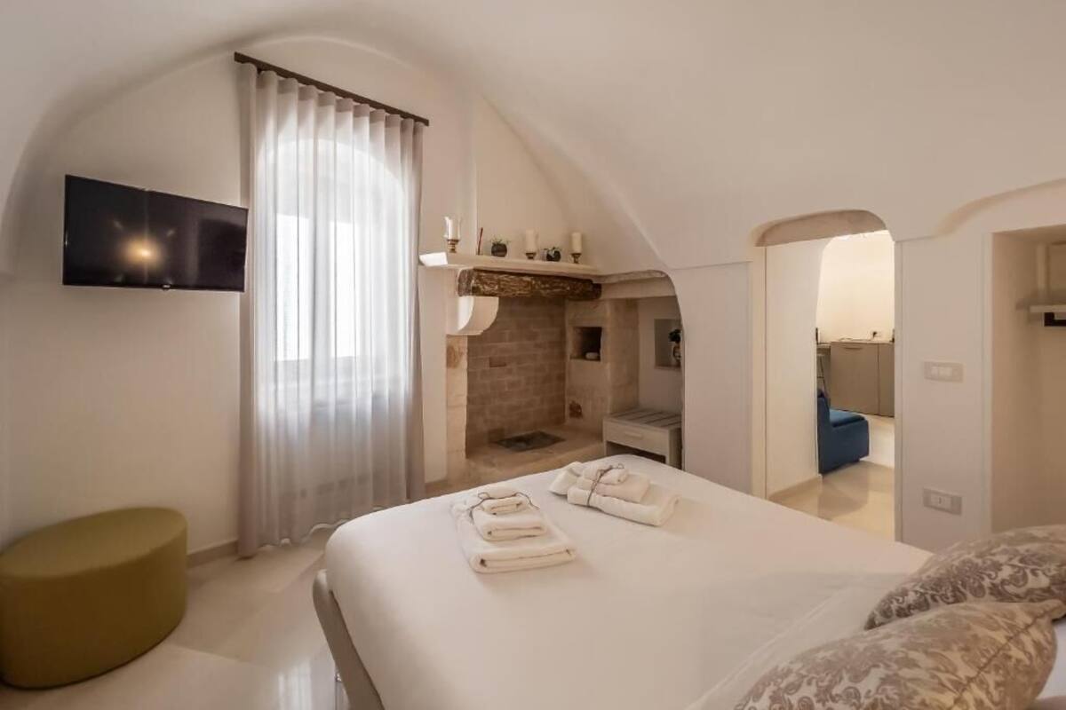 A hotel room with a bed, a TV, a fireplace, and a bathroom visible through an archway.