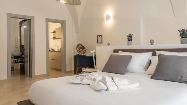 A modern bedroom with a curved ceiling, a bed with neatly folded towels, a bedside table, and a small chair. - DOMUS SAN GIOVANNI (Locorotondo)