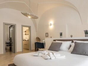 A modern bedroom with a curved ceiling, a bed with neatly folded towels, a bedside table, and a small chair. - DOMUS SAN GIOVANNI (Locorotondo)
