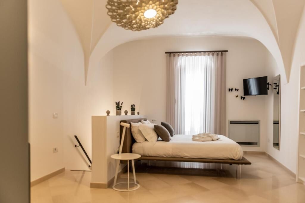 Une chambre à coucher comprenant un lit, une table de chevet, un téléviseur fixé au mur et une fenêtre avec des rideaux.