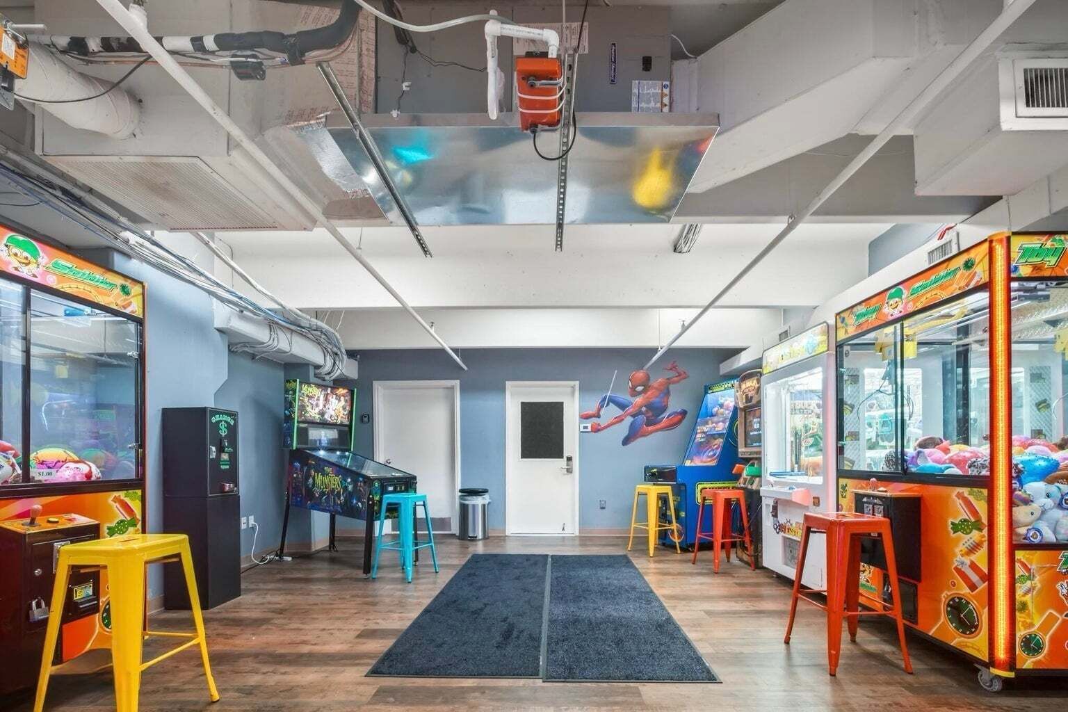 A room with arcade games, a Spider-Man mural, and a door.