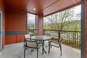 Une terrasse couverte avec une table ronde et quatre chaises, une rambarde et une vue sur un quartier résidentiel.