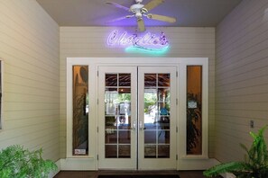 A building entrance with a neon sign reading 'Charlie's' above double doors, a ceiling fan, and potted plants. - Two Separate 2BR Condos w/Pool & Hot Tub (Windsor)