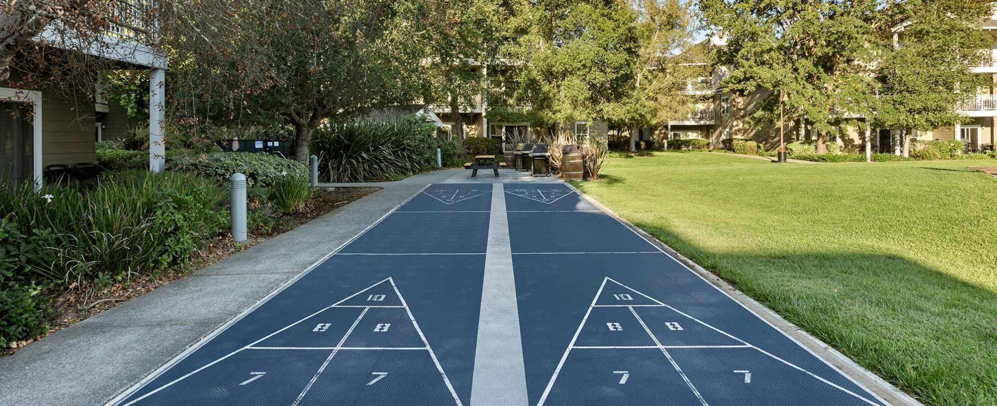 Un campo da shuffleboard con un percorso accessibile, circondato da vegetazione e palazzi residenziali.