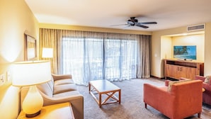 Una camera d'hotel con divano, poltrona, tavolino, televisione e tende.