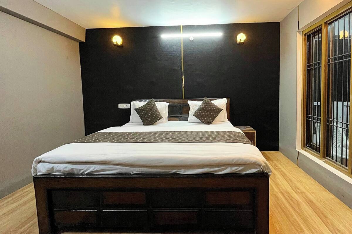 A bedroom with a bed, two wall-mounted lights, a window with bars, and a nightstand.