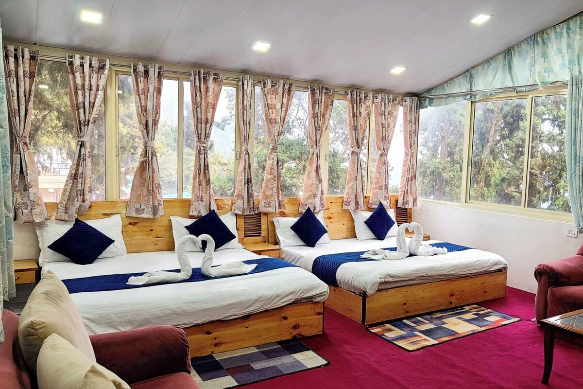 A hotel room with two wooden beds, a red carpet, a wooden chair, and large windows with curtains.