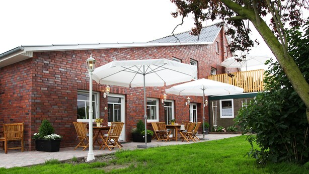 Een gebouw van baksteen met terras, parasols en een tuin.