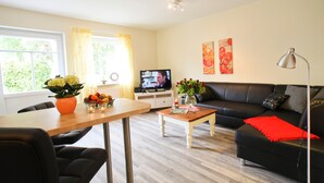 Een woonkamer met een bank, een televisie, een salontafel, en een eethoek met stoelen en een tafel.