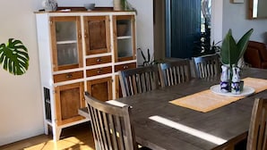 A dining area with a wooden table, chairs, a cabinet with glass doors, and a potted plant. - The tropical farm rural acre with a tropical feel sprawling views 5 mins to town (Ventnor)