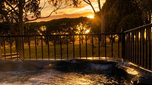 A hot tub with a metal railing, surrounded by trees and a sunset in the background. - The tropical farm rural acre with a tropical feel sprawling views 5 mins to town (Ventnor)
