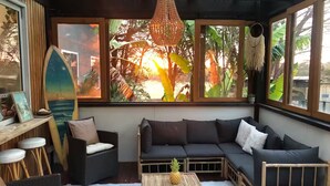 A cozy room with a dark sofa, a small wooden table with a pineapple, and large windows with tropical views. - The tropical farm rural acre with a tropical feel sprawling views 5 mins to town (Ventnor)