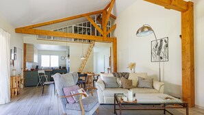 Ein großzügiger Wohnbereich mit hoher Decke, Holzbalken, einer Couch, einem Couchtisch und einem Essbereich mit Treppe.