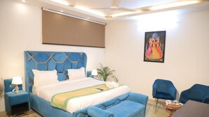 A bedroom with a bed, a desk, chairs, a painting, and a ceiling fan. - Fortune Home Service Apartment D-198 (New Delhi)
