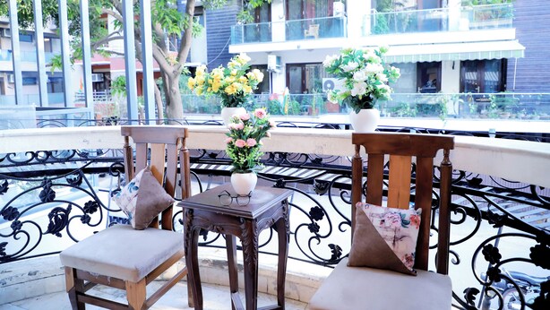 A balcony with two wooden chairs, a small table with a vase of flowers, and a view of a residential building. - Fortune Home Service Apartment D-198 (New Delhi)