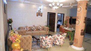 A living room with a sofa, floral armchairs, a coffee table, a chandelier, and a television. - Fortune Home Service Apartment D-198 (New Delhi)